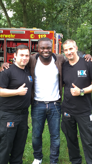 Gerald Asamoah zusammen mit zwei Mitarbeitern des H2K-Teams